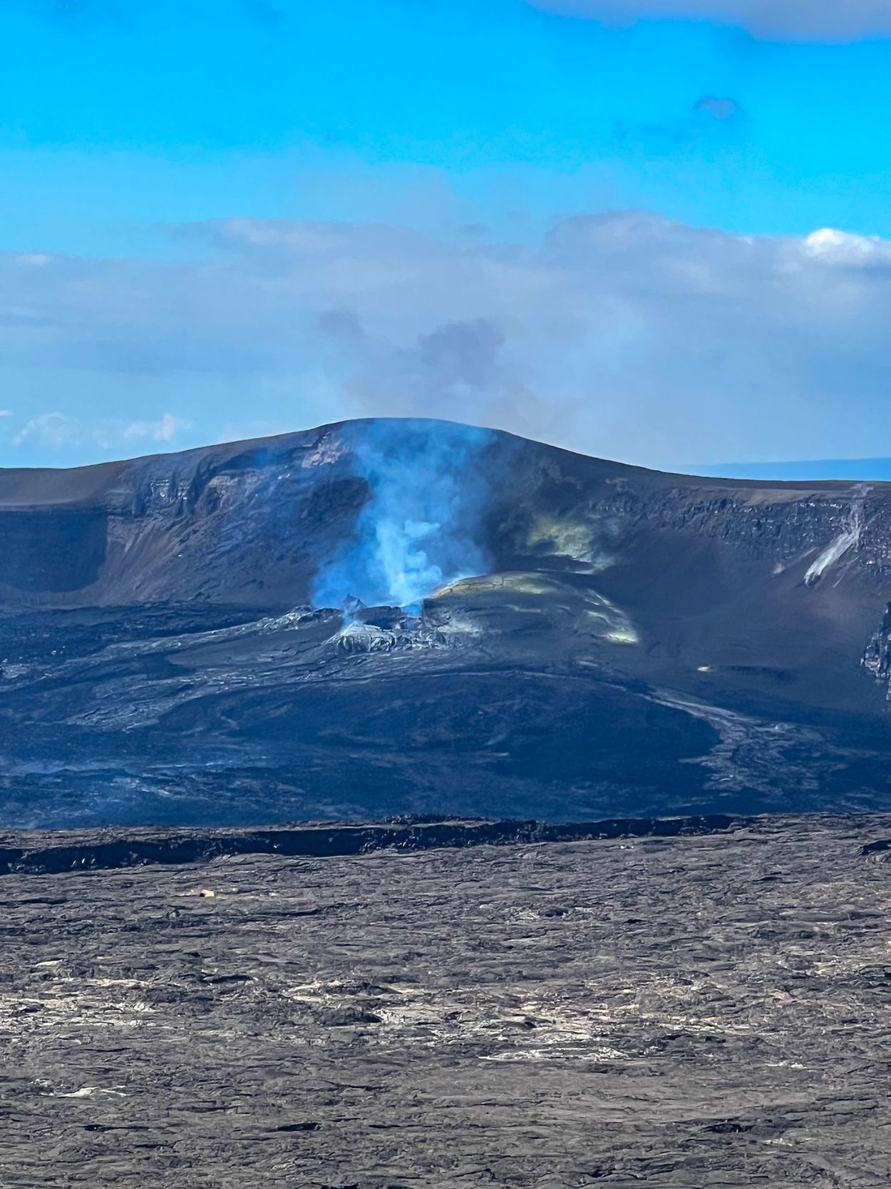 Volcanic crater emitting blue smoke under a clear sky.
