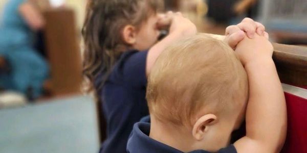 Two young children praying with hands clasped, heads bowed.