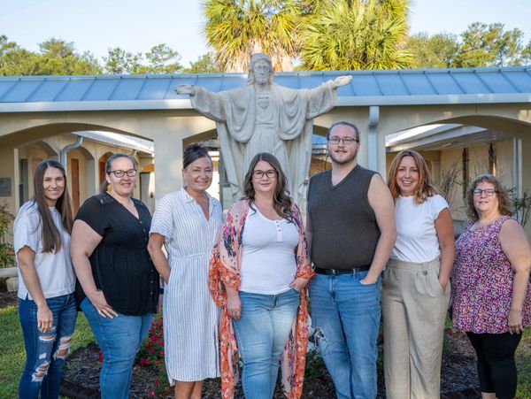 A group of seven people standing in front of a large Jesus statue outdoors.
