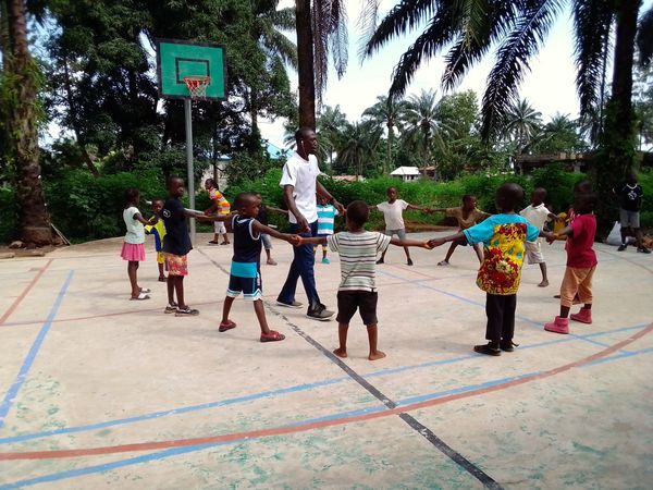 Children and a teacher holding hands in a circle on a basketball court.