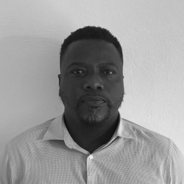 Man posing against a plain wall in black and white photo.