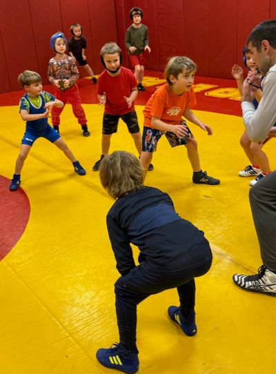 Kids practicing wrestling on a mat with coach.