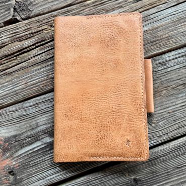 Tan leather journal with pen holder on rustic wooden surface.