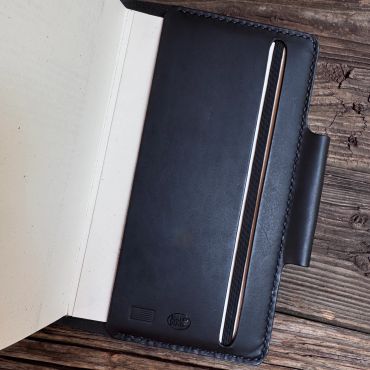 Black leather pen case with a silver pen on a rustic wooden surface.
