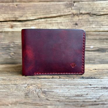 A handcrafted dark red leather wallet on rustic wooden surface.