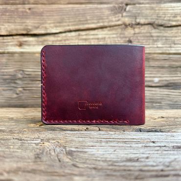A handcrafted burgundy leather wallet on rustic wooden surface.
