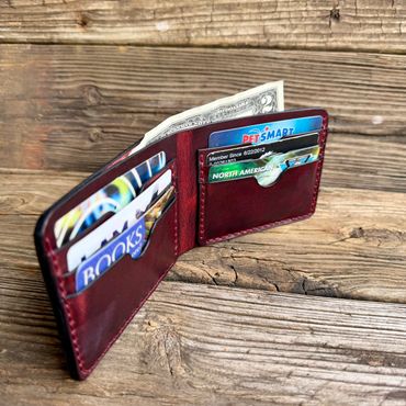 Open leather wallet with cards and cash on wooden surface.