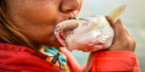 A person kissing a fish she caught, showing affection.