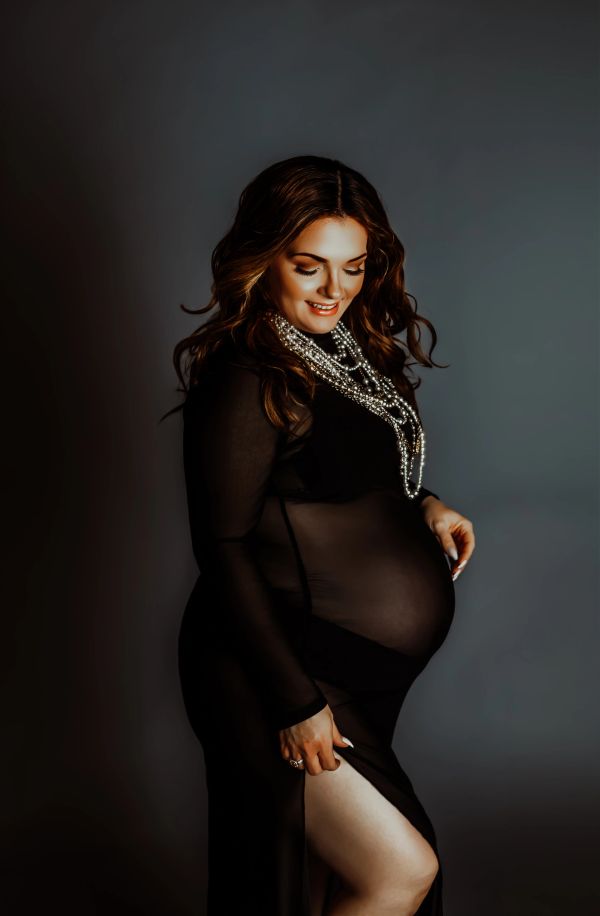 Pregnant woman in a sheer black dress smiling.