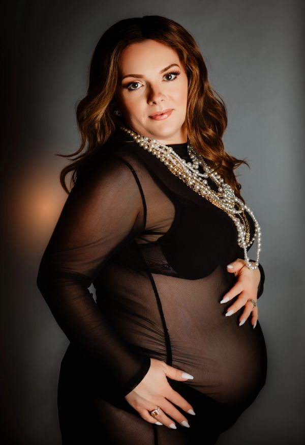 Pregnant woman in sheer black dress with pearl necklace.