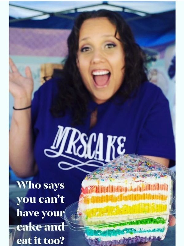 Woman excitedly presenting a colorful layered cake.