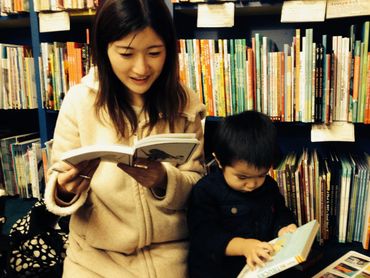 a woman reading a book next to a toddler looking at the cover of a book