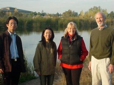 four people standing near a lake