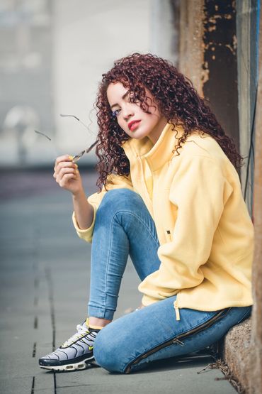 woman sitting down holding glasses, wearing yellow jacket