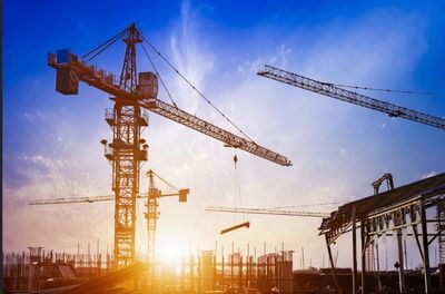 Construction site with cranes at sunset lifting materials.