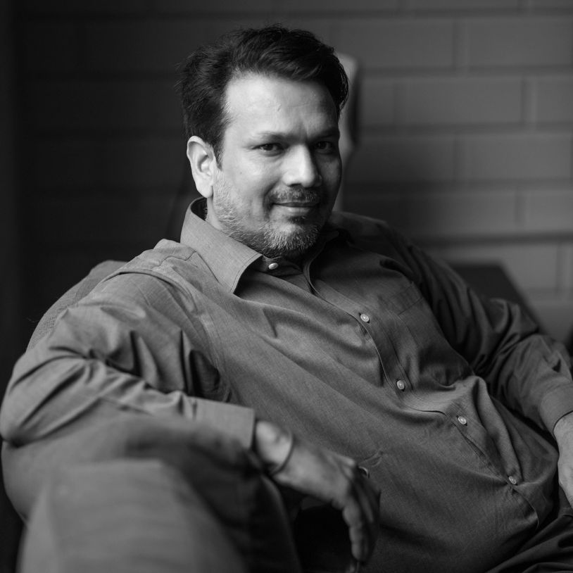 Man in a button-up shirt sitting comfortably on a couch with a slight smile.