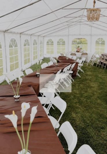 Outdoor tent setup with brown tablecloths and white chairs.