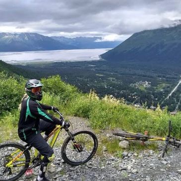 Cyclist overlooking a mountain valley with snow-covered peaks.