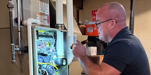 Technician inspecting a furnace in a basement with a flashlight.