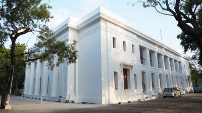 A large white neoclassical building with columns and parked cars.