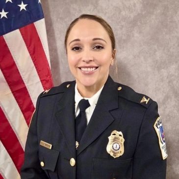 Female police officer smiling with American flag background.