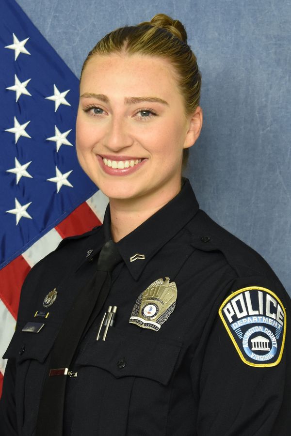 Smiling female police officer in uniform with American flag background.