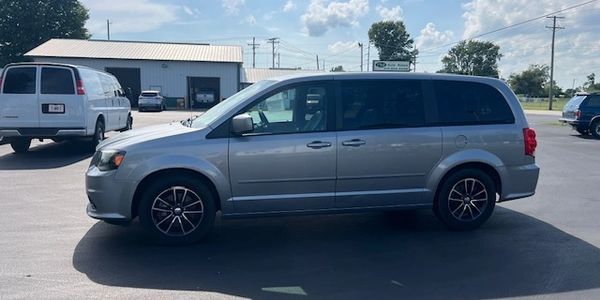 Silver minivan parked in a sunny lot with other vehicles and buildings in the background.