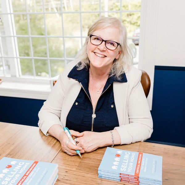 Smiling woman sitting at a table with books about selling homes.