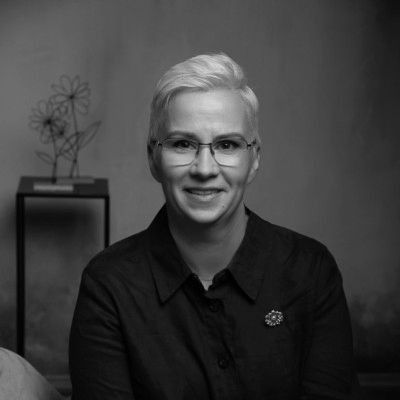 Smiling person with short blonde hair and glasses in a dark blue shirt.