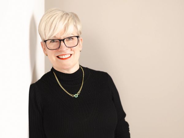 Smiling woman with glasses and short blonde hair in a black top.