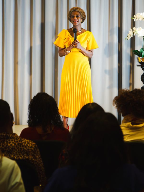 Woman in a yellow dress speaking on stage.