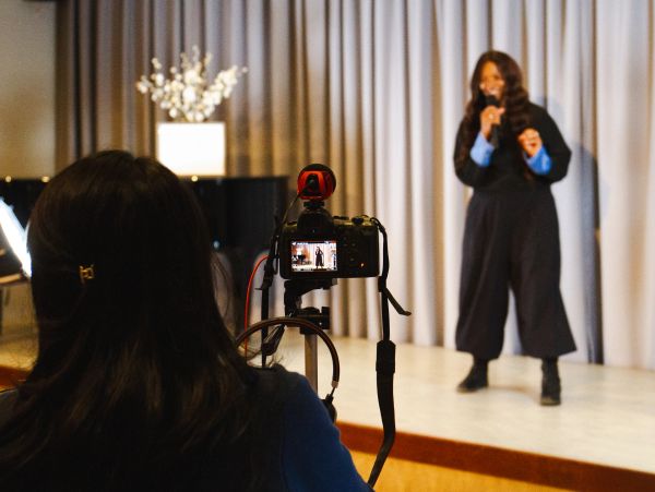Woman speaking on stage recorded by a camera operator.