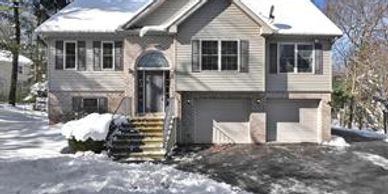 A two-story house with snow-covered roof and yard on a sunny winter day.