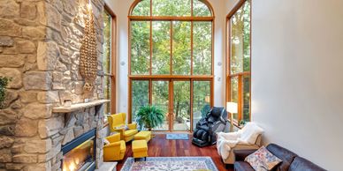 Cozy living room with large windows, stone fireplace, and colorful seating.