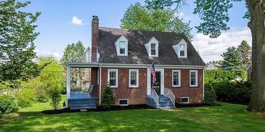Charming brick house with a lush green lawn and large trees.