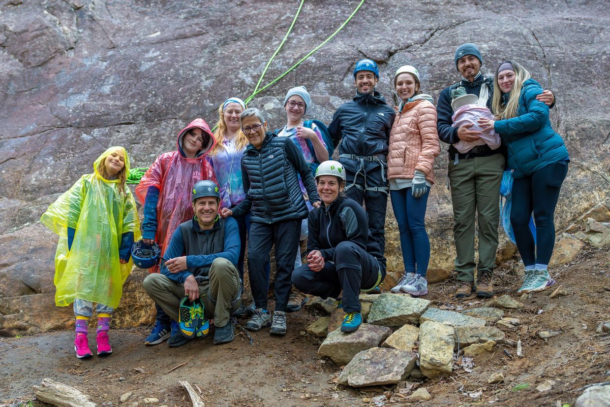 Group of climbers posing in front of a rock wall with gear and helmets.