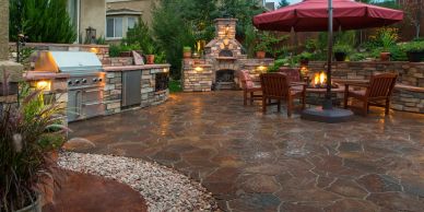 Cozy backyard patio with outdoor kitchen and fireplace under soft lighting.