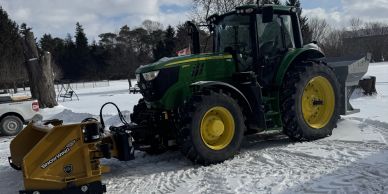 A green tractor with yellow wheels parked on snow-covered ground.