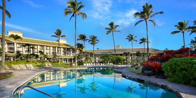 Sunny resort with a clear pool and palm trees under a blue sky.