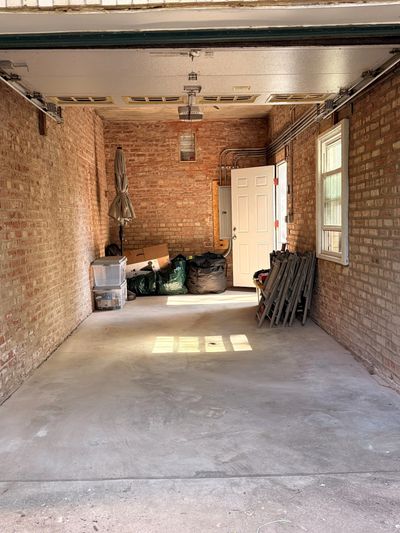 Empty brick garage with storage items at the back and light shining in.