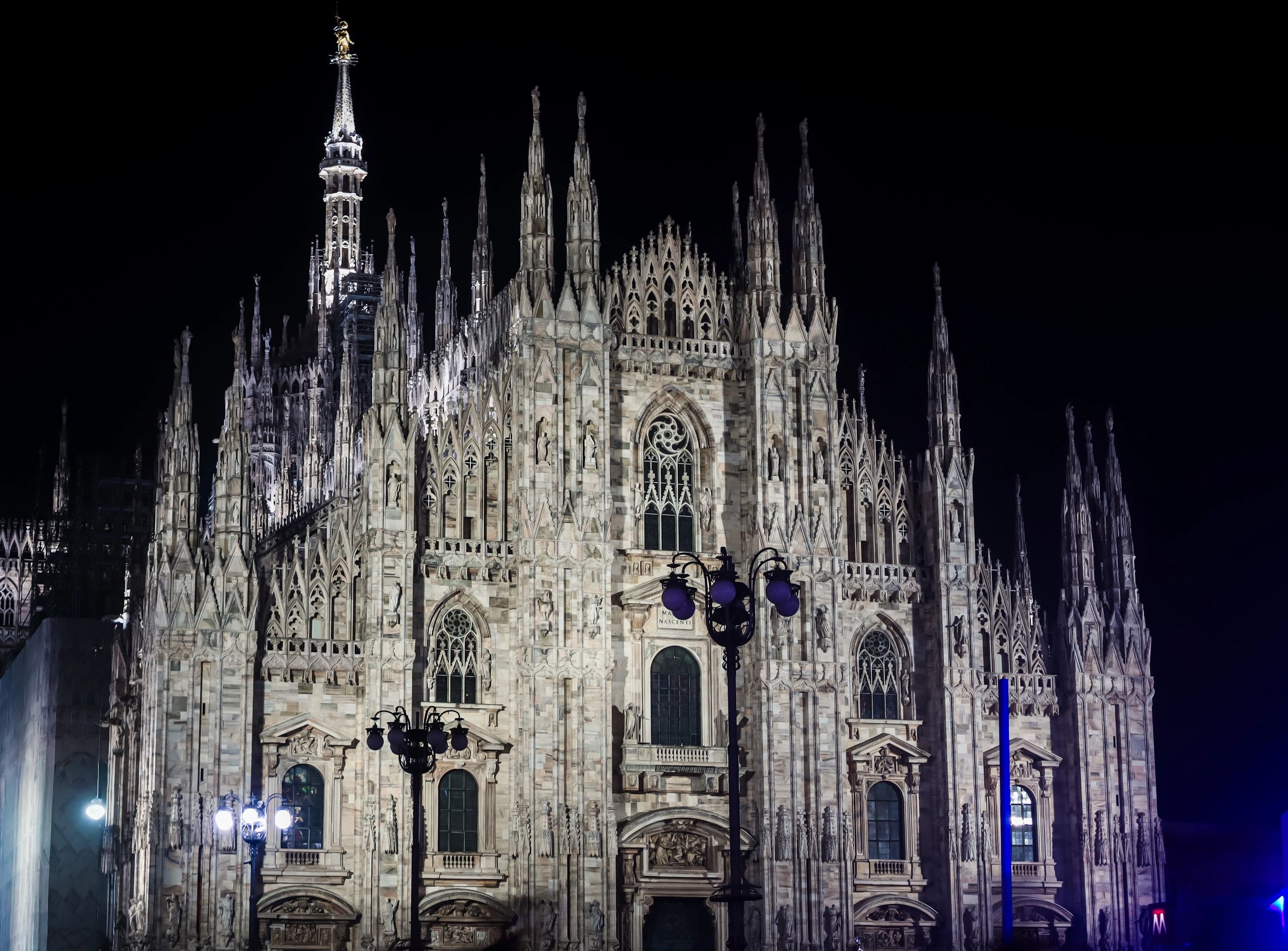 Night view of Milan Cathedral's illuminated Gothic facade.