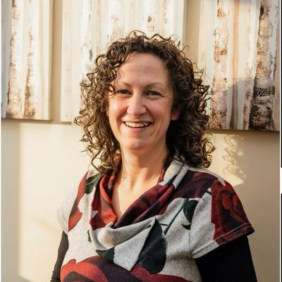 Smiling woman with curly hair wearing a floral patterned top.