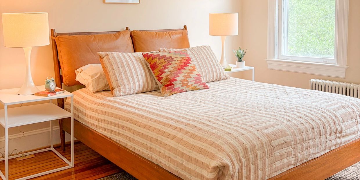 Cozy bed with beige striped bedding and colorful pillow in a bright room.