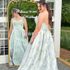 Bride in a pale green floral jacquard strapless ball gown admiring her reflection in a vintage gold mirror with “Welcome to our wedding” written on it.