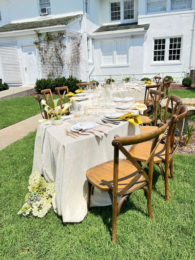 Outdoor wedding table with ivory linens, wooden chairs, gold flatware, and calla lily centerpieces.