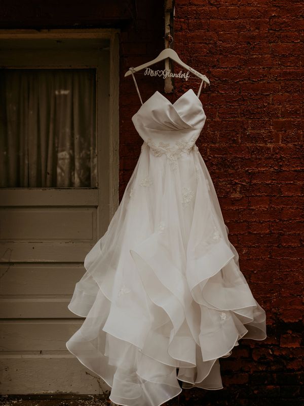 A wedding gown hanging from a hook outside of a brick building.