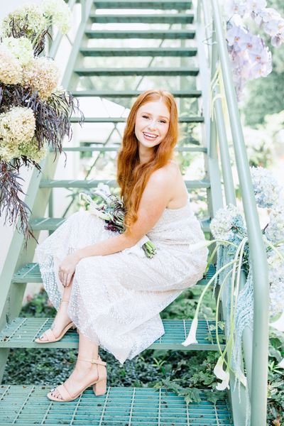 Smiling red-haired woman in a sparkly champagne dress sitting on a green staircase.