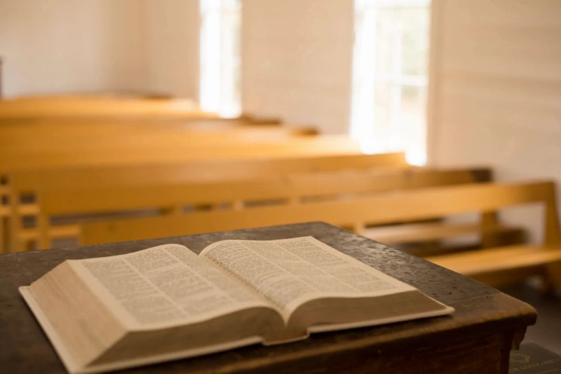 Open Bible on a wooden lectern with empty pews in the background.
