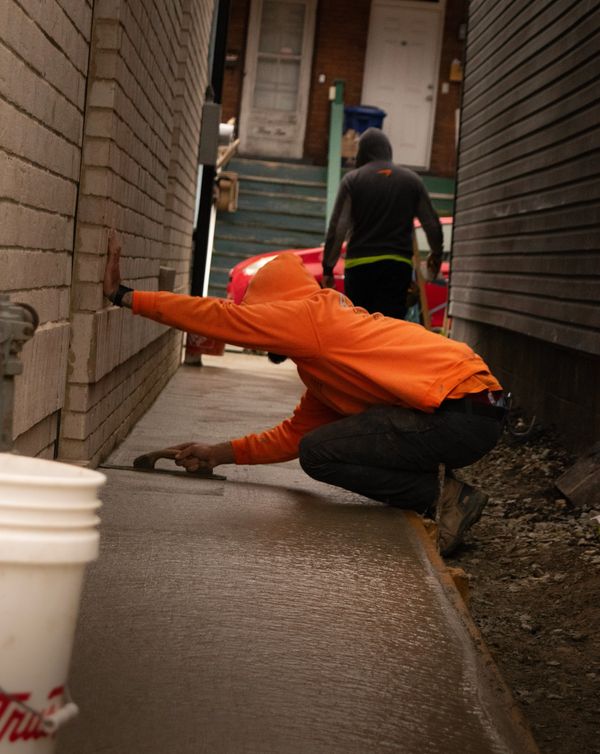 Worker smoothing freshly poured concrete in an alleyway.