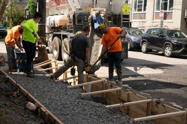 Construction workers pour concrete for a sidewalk on a sunny day.